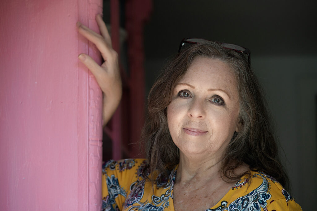 Smiling woman with fair skin leaning against pink wall.