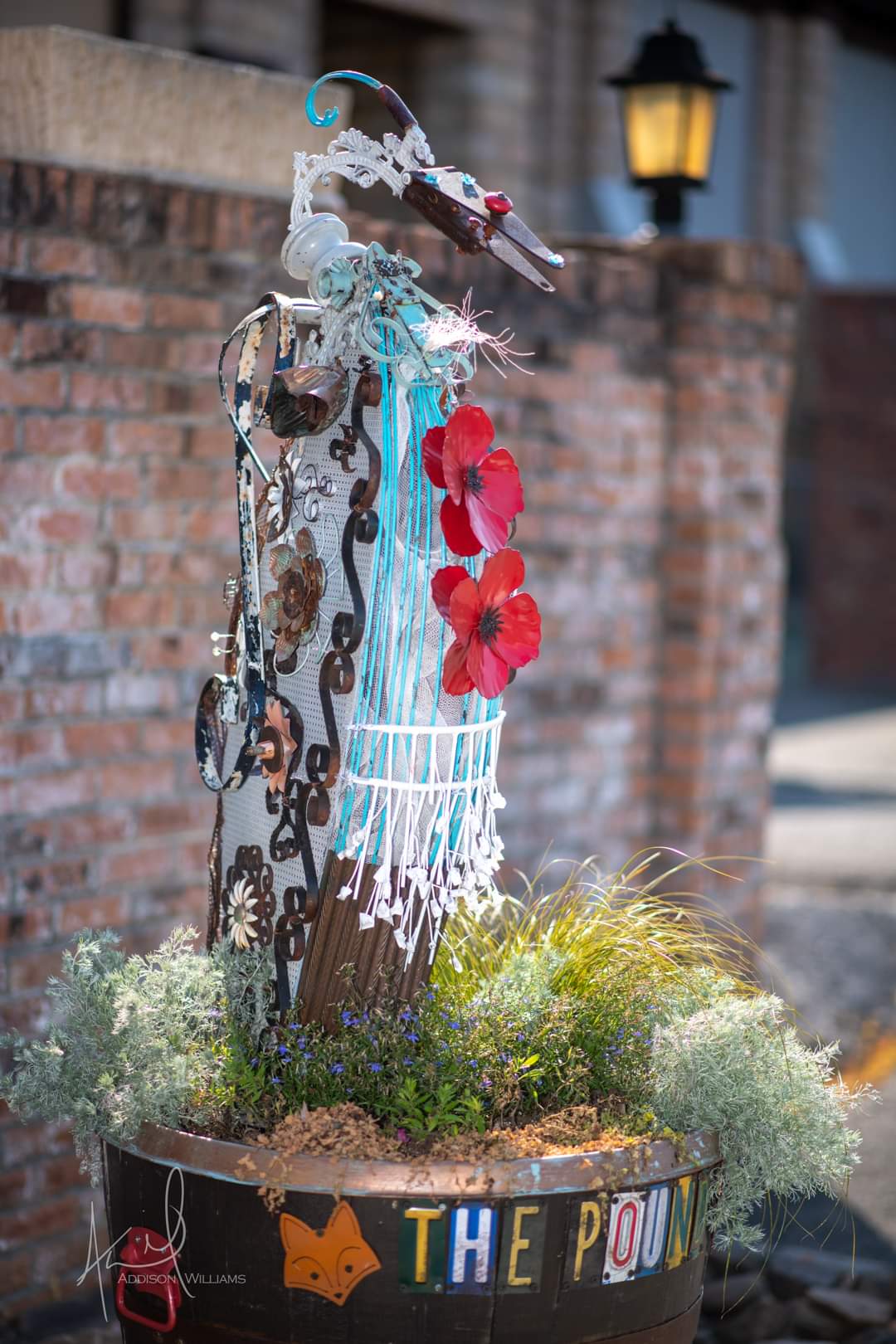 sculpture made from found materials, with red flowers.